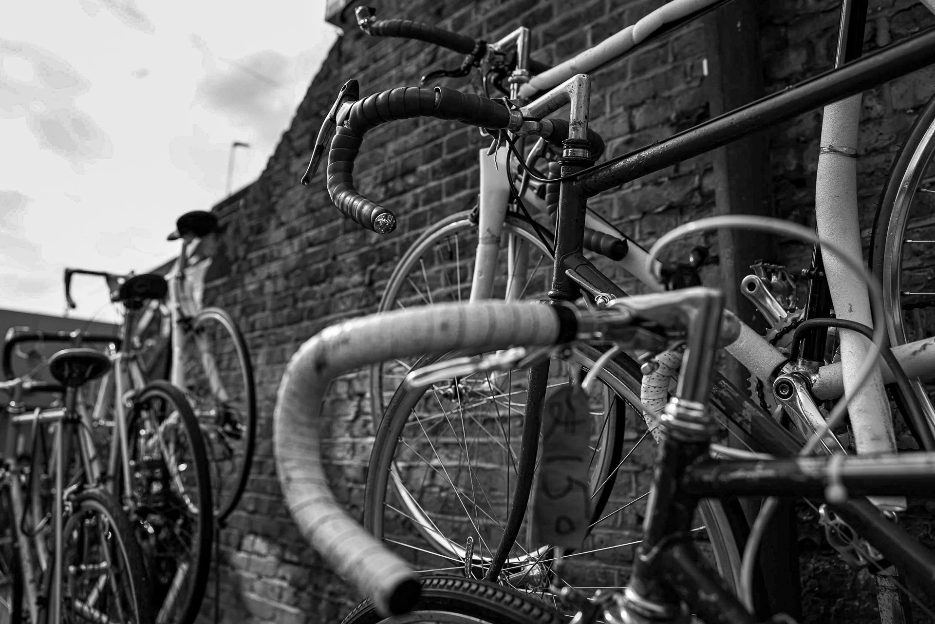 Black-and-white photograph of multiple parked bicycles against a brick wall, capturing metal textures and intricate details. | Canon EOS R5 | RF 28-70mm F2 | 28mm f3.2 | 1/1600s | ISO 100