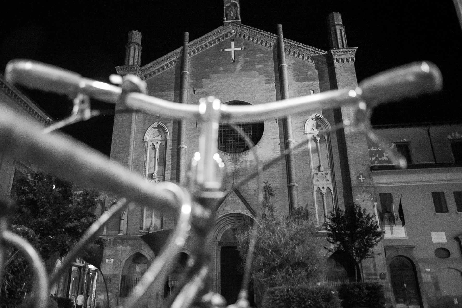Black-and-white shot of a bicycle handlebar framing a historic Italian church façade, blending architecture and cycle details. | Leica SL | N/A | f3.4 | 1/80s | ISO 12500