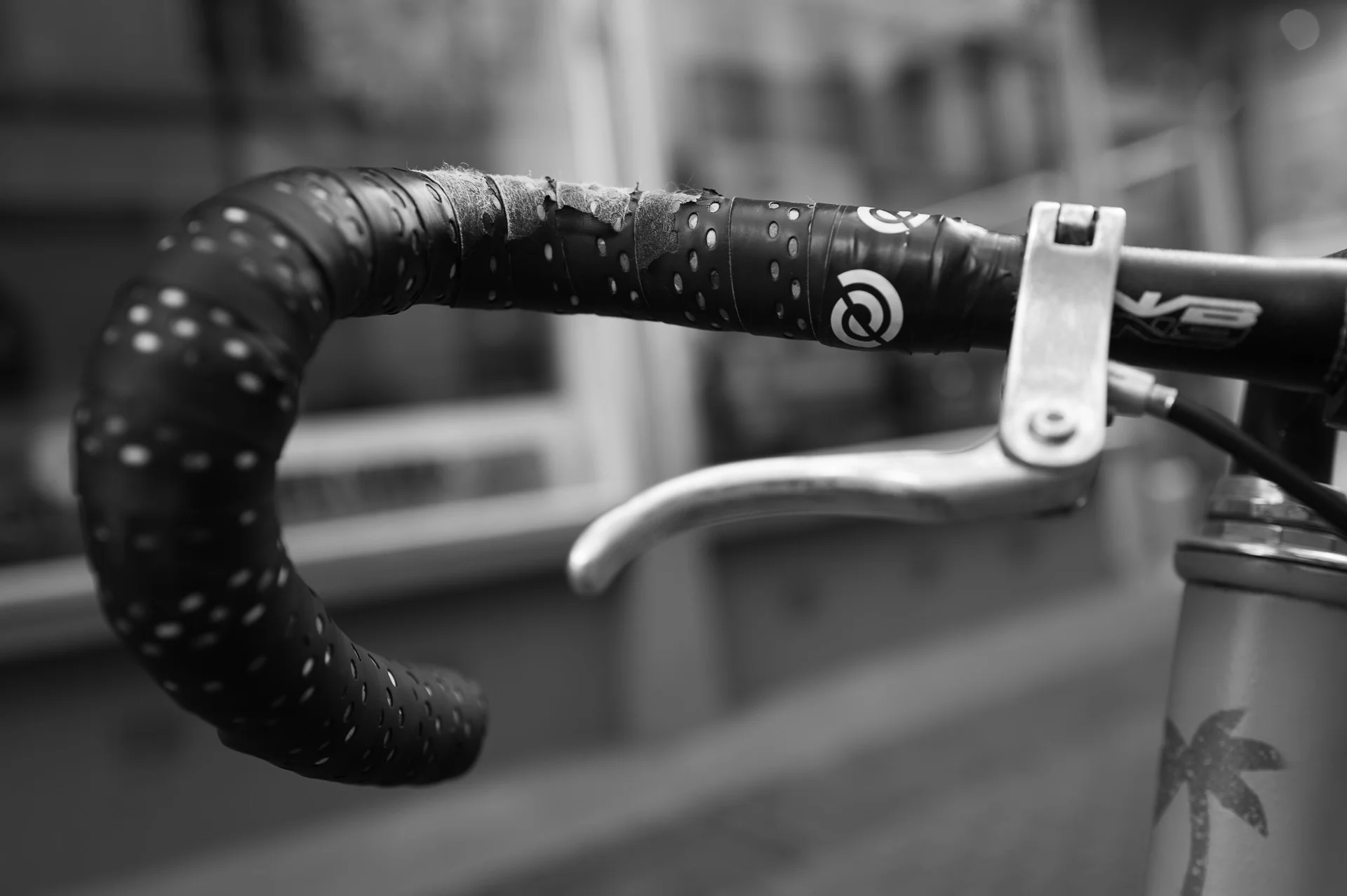 Close-up black-and-white image of a bicycle headlamp with raindrops on the handlebar, emphasizing reflective surfaces. | Leica Q3 | Summilux 28mm f1.7 | 28mm f/2.8 | 1/125s | ISO 125