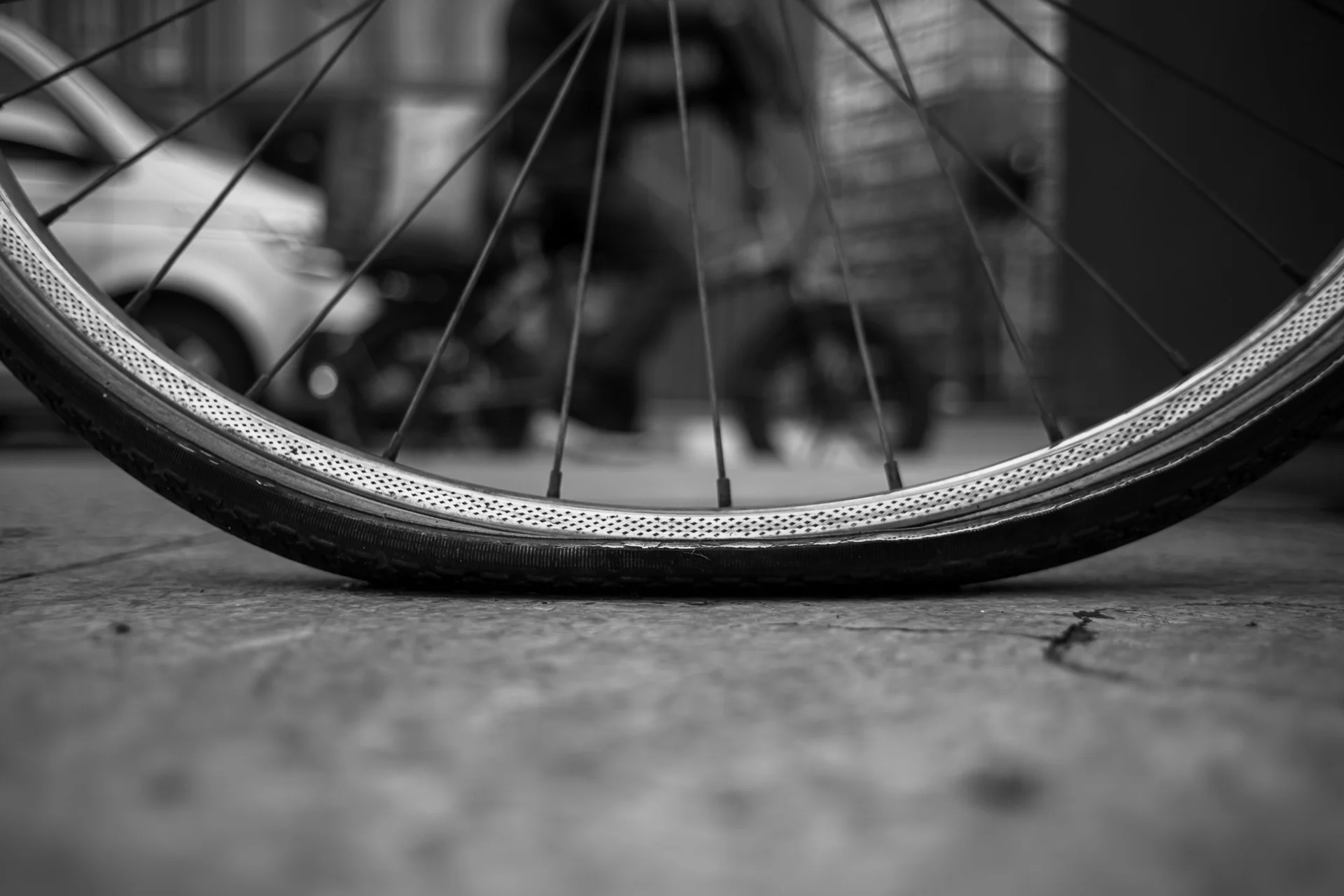 Black-and-white close-up of a bicycle rim resting on concrete pavement, showing textured tire tread and surface contrast. | Leica SL | N/A | f2.8 | 1/125s | ISO 100