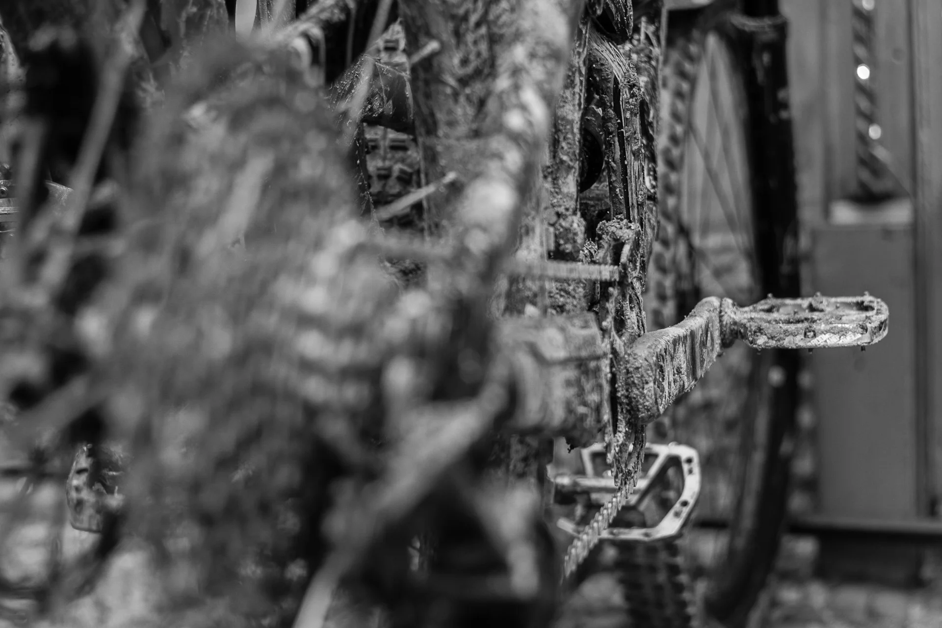 Black-and-white image of a bicycle chain and pedal covered in dried mud, capturing gritty texture. | Leica SL | N/A | f2.8 | 1/800s | ISO 100