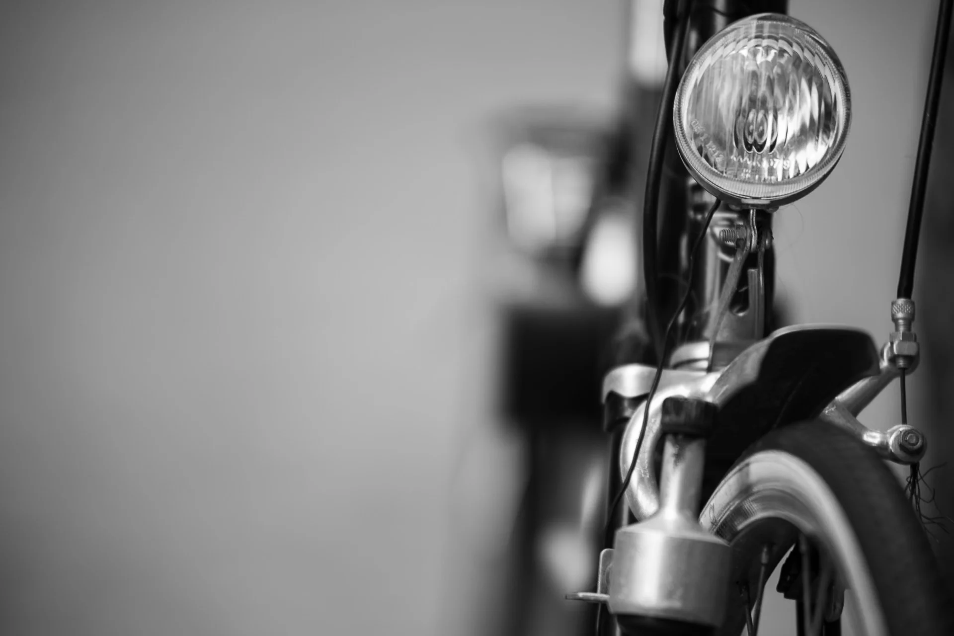 Black-and-white close-up of a bicycle headlamp and front fork, capturing reflective glass and blurred background. | Leica SL | N/A | f2.8 | 1/160s | ISO 100