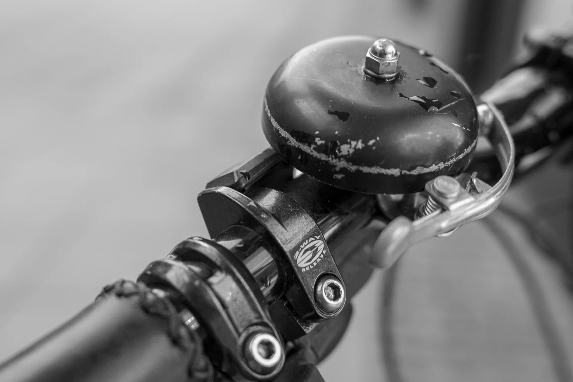 Black-and-white photograph of a bicycle locked to a street post outside a café, with a cyclist riding by in background. | Leica SL | N/A | f2.8 | 1/160s | ISO 100
